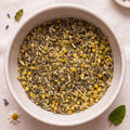 White bowl filled with dried herbs and flowers on a light background