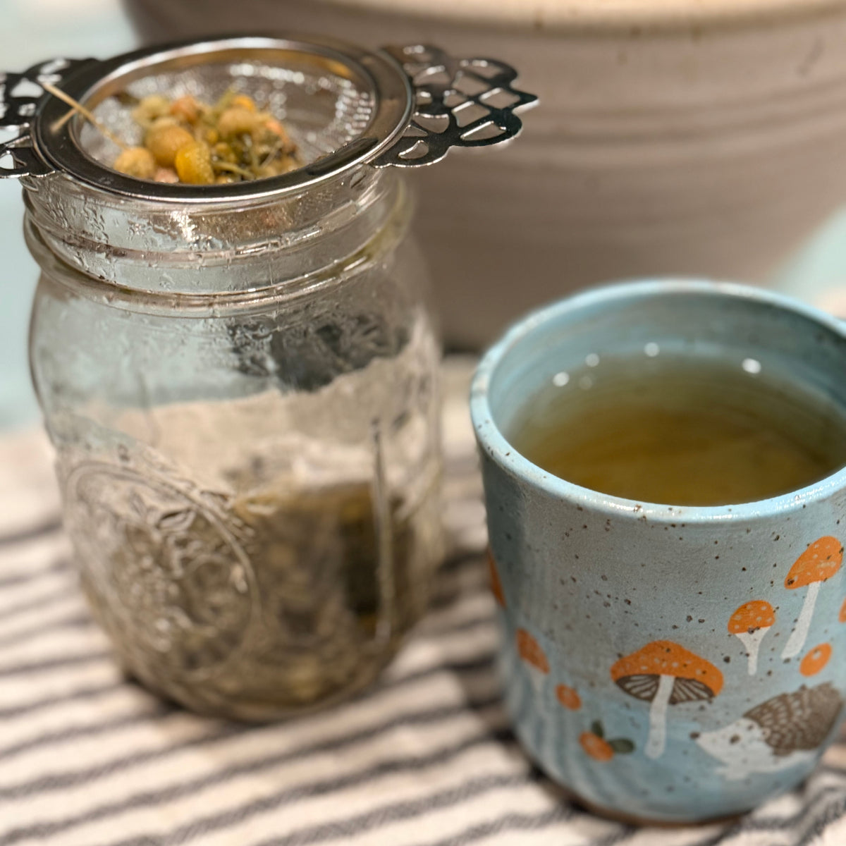 Mason jar with tea leaves and a cup of tea on a striped surface